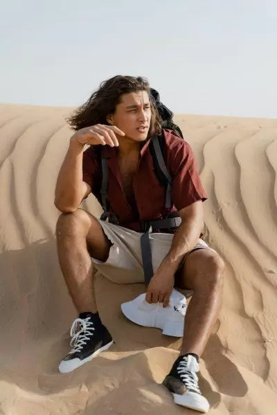 Άντρας στην έρημο του Ντουμπάι ντυμένος με κόκκινο πουκάμισο και μακριά βερμούδα