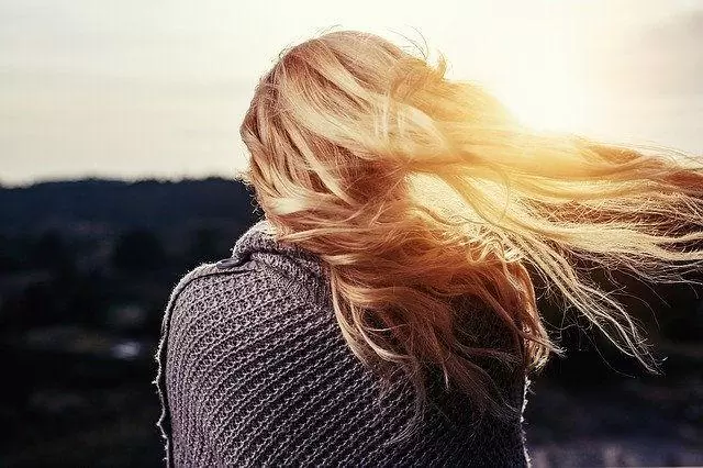 Ξανθιά κοπέλα γυρισμένη πλάτη με φόντο το ηλιοβασίλεμα 